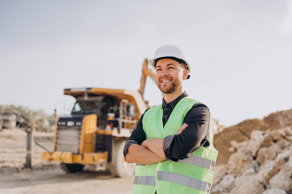 Worker wearing high vis singlet and helmet standing with bulldozer at mine site